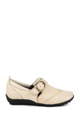 Zapato bajo de cuero color beige con suela negra, detalle de costuras pespunteadas en la puntera y los laterales, y tira ajustable con hebilla metálica dorada en el empeine.