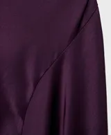Vestido midi de satén color violeta oscuro, con diseño drapeado en el escote y un hombro al descubierto, de manga corta caída y bajo asimétrico.
