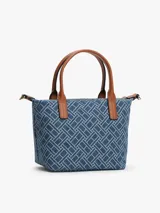 Cartera tote compacta Tommy Hilfiger de tejido denim con estampado geométrico integral del monograma TH, asas superiores en tono marrón y correa de hombro ajustable y extraíble. Cuenta con cierre de cremallera y herrajes dorados.