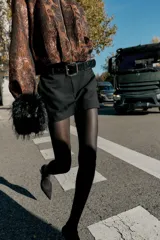 Falda pantalón negra de tiro medio con cierre frontal y hebilla metálica. Presenta bolsillos delanteros y falsos bolsillos de vivo en la espalda.