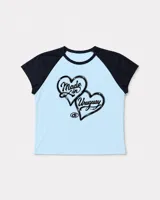 Baby tee de corte ajustado con diseño tipo ranglan, cuerpo en color celeste y mangas cortas en contraste color negro. Presenta un estampado frontal con dos corazones y la leyenda 'Made in Uruguay'.
