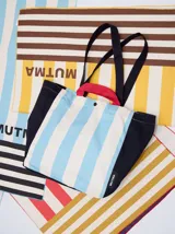 Bolso tipo tote con diseño de rayas verticales en amarillo y blanco, con laterales, base y correas en color marrón. Incluye asas cortas en color naranja y cierre con botón a presión.