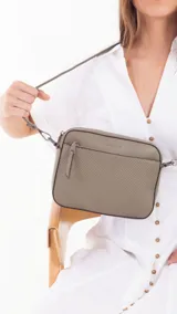 Bandolera color bordó con diseño texturizado geométrico en el frente, bolsillo frontal con cierre, bolsillo trasero con cierre y compartimento principal con divisiones. Incluye correa extensible.