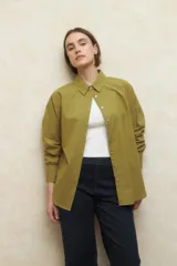 Camisa de corte clásico y holgado, confeccionada en tela blanca, con cuello camisero, cierre frontal de botones de nácar y mangas largas con puños abotonados.