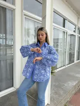 Camisa de corte holgado en color azul con bordado floral blanco tipo broderie. Presenta cuello clásico, cierre frontal con botones y mangas largas abullonadas con puños ajustados.
