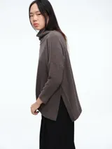 Buzo tejido de cuello alto, con diseño de sisa caída y silueta holgada. Presenta aberturas laterales en el ruedo que aportan movimiento.