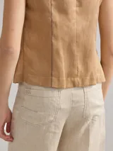 Chaleco sin mangas de lino, con diseño de paneles en color blanco crudo y beige. Presenta escote redondo y cierre frontal con botones de madera marrones.