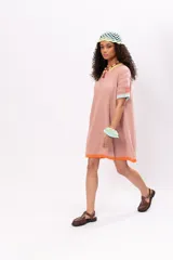 Vestido corto tejido de punto color salmón, con cuello redondo y mangas cortas. Presenta ribetes en color amarillo en el cuello, celeste en las mangas y naranja en el ruedo.