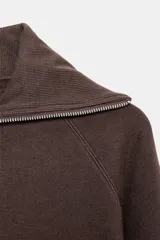 Chaqueta de felpa negra con cuello solapa, manga larga con puño, bolsillos de plastrón en el delantero y cierre frontal con cremallera.