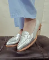 Mocasines de cuero plateado con acabado texturado, diseño clásico con costuras visibles y vira de suela natural cosida. Cuenta con taco plano de 2 cm y plantilla anatómica.