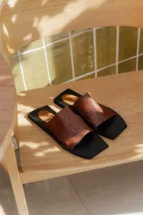 Sandalias planas con punta cuadrada, base negra y capellada de cuero marrón con textura trenzada.