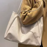 Bolso tipo tote bag color beige claro, de material sintético liso con caída suave. Posee dos asas delgadas para llevar al hombro.