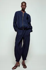 Pantalón de tiro alto de tela satinada color azul marino, con bolsillos frontales, cintura ajustable con cordones y puños elásticos en los tobillos.