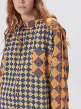 Camisa de viscosa con estampado de rombos en tonos tierra, azul y rojo. Presenta cuello clásico, cierre frontal con botones, bolsillo delantero cuadrado y logo bordado. De corte holgado y manga larga.