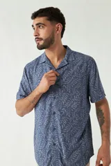 Camisa de manga corta con cuello cubano, confeccionada en viscosa con estampado de hojas en tonos azules. Presenta cierre frontal abotonado y corte slim.