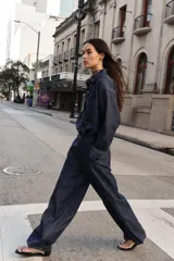 Jeans de tiro alto color azul oscuro, con cintura elástica en la espalda, bolsillos delanteros y bolsillos de plastrón en la espalda. Presenta pernera ancha y cierre frontal con cremallera y botón a presión.