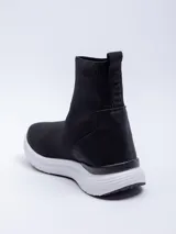 Zapatilla negra de textil elastizado, de caña media y calce tipo media. Detalle de pieza de PU en el talón.