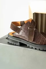 Sandalias de plataforma con suela track, confeccionadas en una combinación de cuero liso y cuero con textura croco. Presentan tiras anchas en el empeine y cierre con hebilla ajustable en el talón.