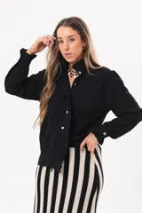 Camisa de manga larga color negro, con cuello camisero, cierre frontal con botones y detalle de volados en la cartera y los puños.