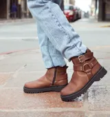 Botas de caña baja color chocolate, realizadas en cuero encerado, con hebillas en la caña y herrajes de níquel. El fondo es de suela negra realizado artesanalmente y el interior está forrado en forrería vacuna.