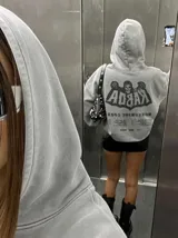 Canguro de felpa gris melange con capucha, manga larga y estampa trasera de estilo rockero con tipografía y calavera.