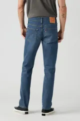 Jean de corte slim fit con tiro bajo, confeccionado en denim azul con efecto de lavado desgastado. Presenta cierre de botones y remaches metálicos clásicos.