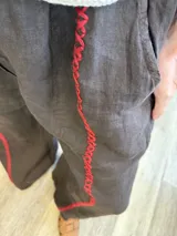 Pantalón ancho de lino color tostado, con cintura elástica y detalles de bordado rojo a lo largo de las piernas.