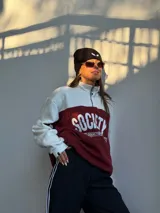 Buzo de estilo deportivo con diseño de bloques de color en blanco y bordó. Presenta cuello alto con medio cierre frontal, mangas largas con puños acanalados y estampado gráfico frontal con la palabra Society.
