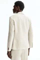Blazer de lino liviano color beige, con solapas de muesca finas, botonadura sencilla de un botón, bolsillos con solapa en el frente y bolsillo superior ojal.