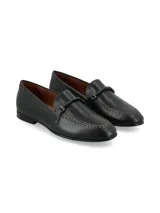 Mocasín de estilo tailor en cuero negro, con costuras marrones visibles alrededor de la puntera y una tira superior con hebilla forrada.