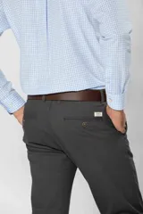 Pantalón de gabardina color marrón claro, corte slim fit, con bolsillos laterales y traseros. Se ajusta a la cintura con cinturón de cuero marrón.