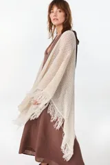 Ruana de punto color beige con diseño abierto y flecos en los bordes.