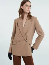 Blazer sastrero color tostado con solapas clásicas, cierre frontal de doble botonadura y bolsillos con solapa. Presenta mangas largas con botones decorativos en los puños.