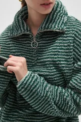 Buzo de textura afelpada con diseño de rayas horizontales finas en tonos marrones. Presenta cuello alto con cierre frontal parcial y mangas largas holgadas.