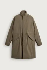 Parka de corte relajado confeccionada en tejido técnico color verde militar, con cuello alto, manga larga con puño ajustable y bolsillos con solapa en la cadera. Cuenta con cintura ajustable mediante cordones internos y cierre frontal oculto con cremallera y botones a presión.