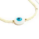 Pulsera de acero con cuentas pequeñas color crema y cuentas doradas. En el centro tiene un dije redondo con un ojo turco.