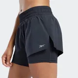 Short de running Reebok 2 en 1, color negro, con calza interior integrada y cintura elástica. Presenta un diseño con dobladillo solapado y logo reflectante en la pierna.