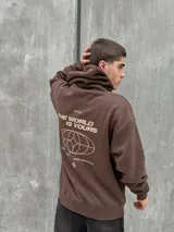 Canguro marrón con capucha ajustable con cordones, bolsillo tipo canguro y puños elásticos. Presenta un logo de un globo terráqueo y una flor bordados en el pecho.