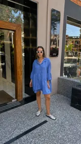 Vestido corto de manga larga con volados, color lavanda, con cuello camisero y botones frontales.