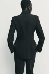 Blazer de corte estructurado con hombreras, cuello solapa y manga larga. Presenta un diseño cruzado con cierre frontal de botones y bolsillos delanteros con solapa.