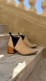 Botinetas de cuero color beige claro con inserciones elásticas laterales en negro y taco cuadrado de madera. Presentan punta fina y tirador trasero.
