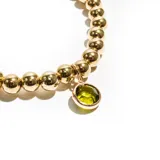 Pulsera elástica dorada con cuentas redondas y dije colgante de cristal facetado color verde claro.