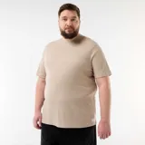 Camiseta de manga corta en color beige, confeccionada en tejido de punto acanalado con sutiles rayas horizontales y cuello redondo. Cuenta con una pequeña etiqueta decorativa en el borde inferior.
