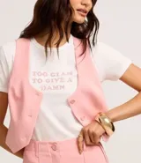 Remera de algodón blanca con cuello redondo y mangas cortas. Presenta una estampa frontal con la frase 'Too glam to give a damn' decorada con strass rosados y detalles de pliegues en los hombros.