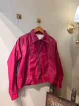 Campera corta color fucsia, con cuello camisero, cierre frontal con cremallera y costuras decorativas en hilo blanco.