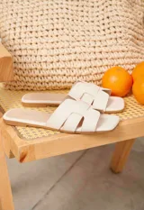 Sandalias planas tipo chinela color camel, con diseño de tiras entrelazadas en forma de "H" y punta cuadrada.
