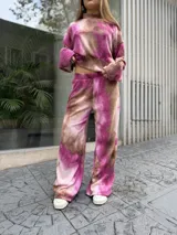 Conjunto de dos piezas compuesto por un buzo corto de manga larga y un pantalón de pierna ancha, confeccionado en tela morley elastizada con estampado tie-dye en tonos fucsia y marrón.
