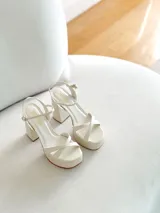 Sandalias de cuero sintético color manteca, con plataforma y tacón bloque. Presentan tiras cruzadas en el empeine y pulsera con hebilla al tobillo.