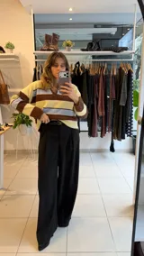 Sweater tejido de punto con diseño a rayas horizontales en tonos amarillo, celeste y marrón. Presenta un cuello polo con escote en V, mangas largas y un corte holgado.