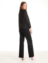 Blusa negra de gasa con cuello a la base fruncido, mangas largas amplias con puños elastizados y apliques de cinta con tachas en la parte delantera y antebrazos. Tiene una abertura central en la espalda con botón.